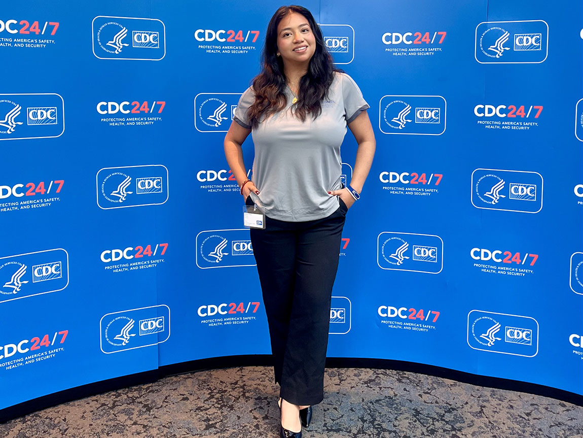 A college student poses in front of a background that has the Centers for Disease Control and Prevention logo on it